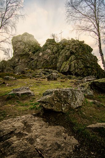 A vertical shot of a cross on the top of rocks on a sunset sky background