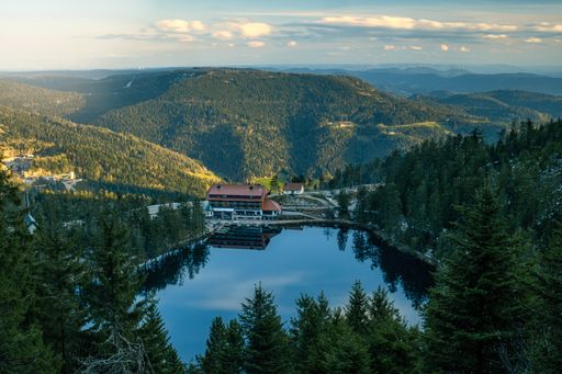 A scenic view of a lake surrounded by forests on a cloudy sky background
