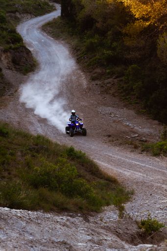 Man on the blue ATV Quad on off road track on the mountains raising a lot of dust, people outdoor sport activities theme
