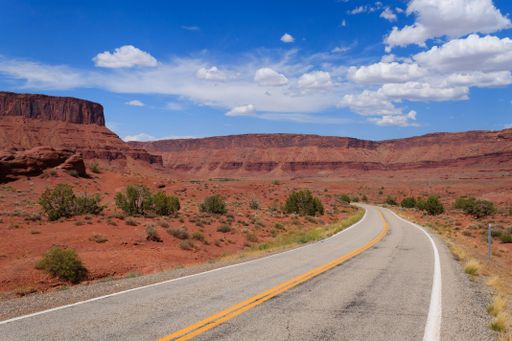 A scenic road winding through the red rock desert landscape under a clear blue sky in Utah.