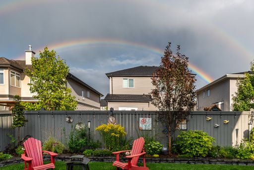 Rainbow over houses in a neighborhood and pink chairs in a yard of a house