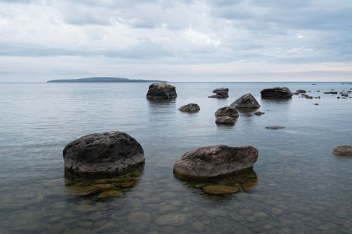 A tranquil seascape with large rocks in the foreground and an island in the distance under a cloudy sky in Awenda Provincial Park, Ontario Canada