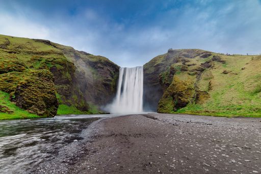 A scenic view of Skogafoss waterfall in Iceland with green cliffs and a blue sky.