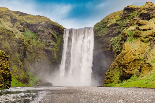A beautiful view of Skogafoss waterfall in Iceland with lush green cliffs and a blue sky
