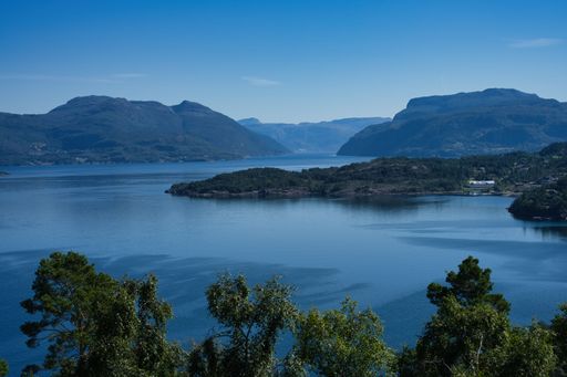 Scenic view of a fjord surrounded by mountains under a clear blue sky in Norway.