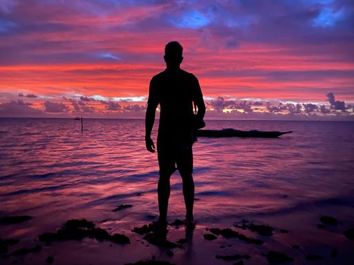 Silhouette of a man standing on the beach during a vibrant sunset with colorful sky and calm ocean