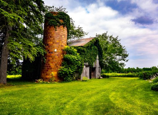 An old barn with a silo covered in ivy on a lush green farm under a partly cloudy sky. Michigan