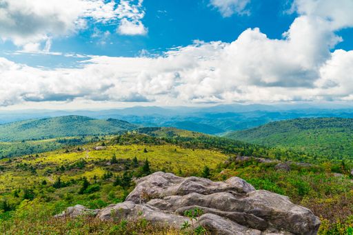 A scenic view of lush green mountains under a blue sky in Grayson Highlands State Park, Virginia
