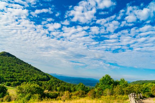 A scenic view of lush green mountains under a blue sky in Grayson Highlands State Park, Virginia