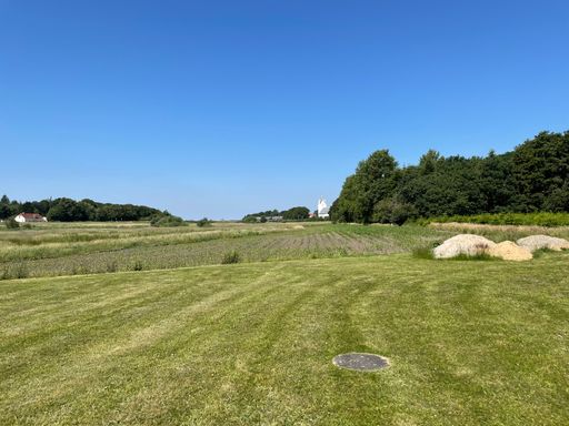 A scenic view of a grassy field with a distant house under a clear blue sky on a sunny day.