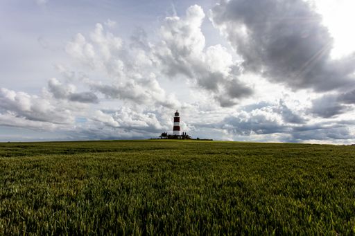 A Beautiful scenery of a green field and Happisburgh Lighthouse on the horizon under cloudy sky in UK