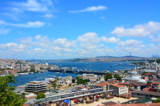 Panoramic view of Istanbul with the Bosphorus Strait, featuring boats and cityscape under a bright blue sky with scattered clouds