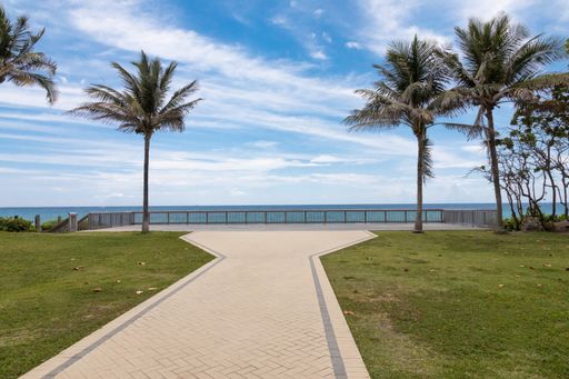 Landscape view of a walkway to the Ocean in Deerfield Beach Florida lined by palm trees.