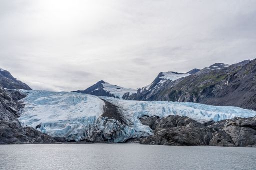 A stunning view of a glacier with snow-capped mountains and a cloudy sky in the background