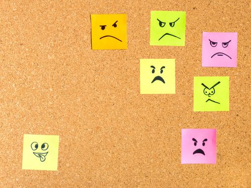 Colorful sticky notes with various hand-drawn facial expressions on a corkboard