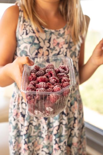 A vertical shot of a woman in a butterfly dress holding a tin of raspberries with her head out of the frame