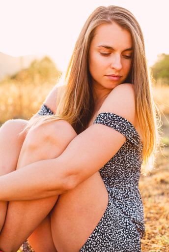 A beautiful young female with long blonde hair wearing a light dress in a field