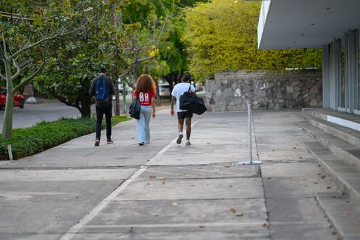 The three young people walking on a sidewalk near a modern building in Guadalajara