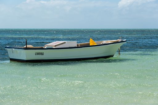 A small white boat anchored in clear turquoise waters on a sunny day with a blue sky