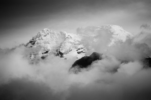 A grayscale shot of mountains covered in snow and clouds
