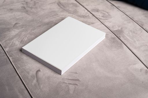 A book with blank cover on gray velvet sofa backdrop, editable mock-up series template