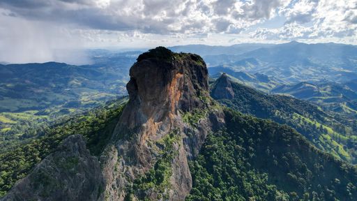 A stunning aerial view of Pedra do Bau in Sao Bento do Sapucai, Brazil, with lush green hills and a dramatic cloudy sky