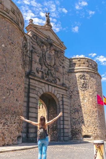 A vertical shot of a female traveler at the Puerta de la Bisagra (Gate of Bisagra) in Toledo, Spain.