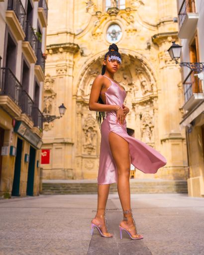 a Dominican ethnic girl with braids wearing a beautiful pink dress standing by the city church