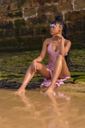 a young Dominican female in a beautiful pink dress and braids enjoying summer sitting on the beach