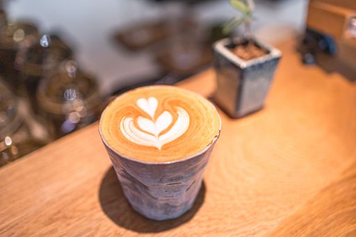 A close-up shot of a beautifully crafted latte with latte art in a ceramic cup on a wooden table in a cozy cafe.