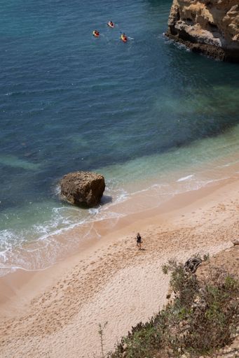A scenic view of a sandy beach with rocky cliffs and clear blue water in Algarve, Portugal