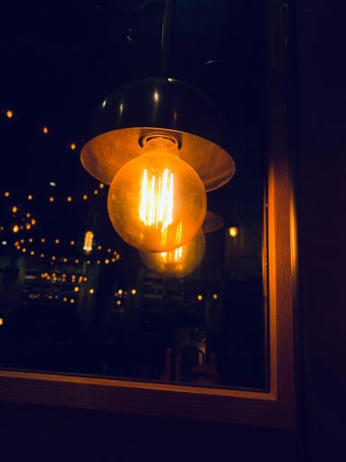 A close-up of a vintage light bulb with a warm glow, reflecting on a glass surface