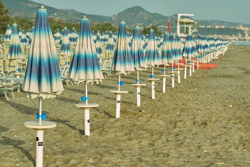 A row of closed beach umbrellas and chairs on a sandy beach with mountains in the background