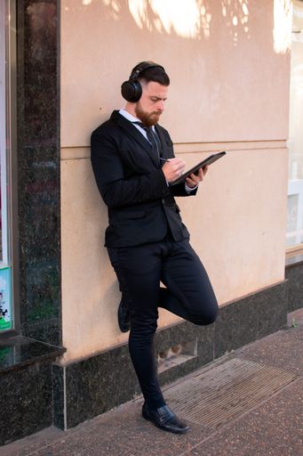 A young Hispanic male in an elegant suit and big headphones using a tablet