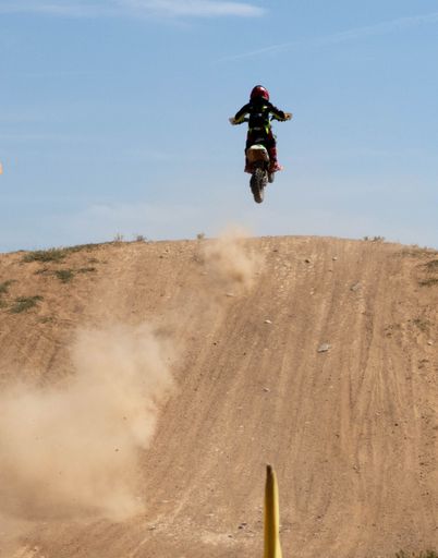 A motocross rider in mid-air during a jump on a dirt track under a clear blue sky.