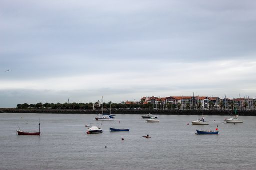 A beautiful gloomy day at the sea with small boats floating on the water and houses far in the back