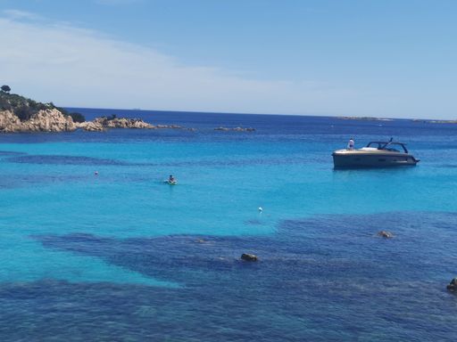 A serene coastal scene with clear blue waters, a boat, and rocky shores in Fano, Italy