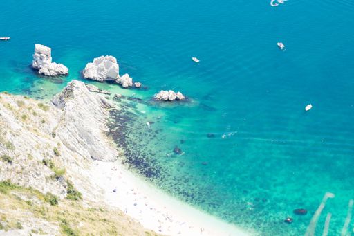 Aerial view of a beautiful rocky coastline with clear turquoise waters and boats near a sandy beach.
