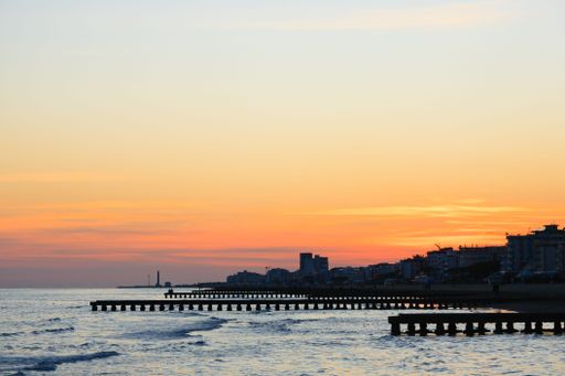 A serene sunset over a coastal city with piers extending into the calm sea and a colorful sky.