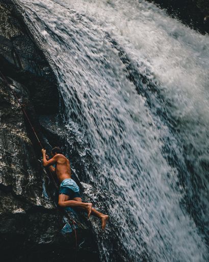 A vertical shot of a man climbing Harper Creek Falls in NC, the USA