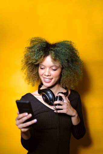 A vertical shot of an African American woman looking at her phone on an orange background
