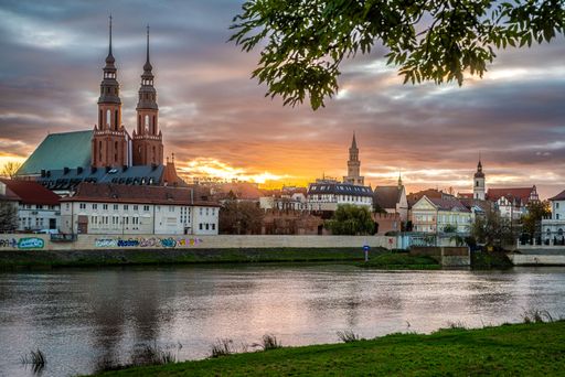 A scenic view of Opole, Poland at sunset with historic buildings and a river in the foreground