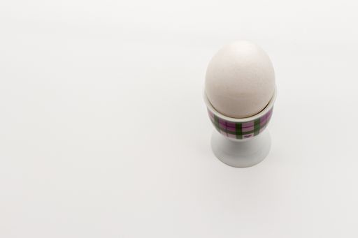 A closeup shot of a white egg in a patterned cup on a white background