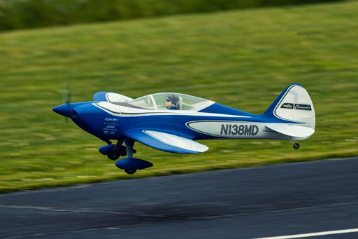 A blue and white model aircraft in flight over a grassy field