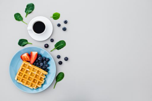 A top view of waffles with different berries and a coffee mug isolated on a light-colored background