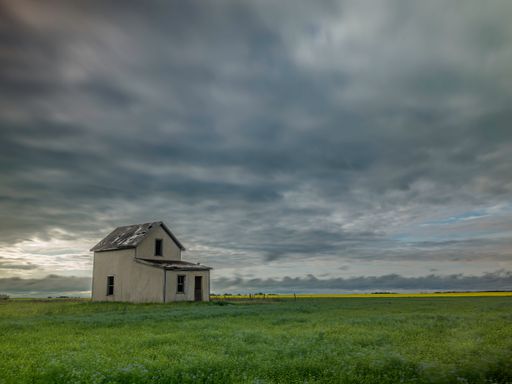An abandoned house in a vast green field in Aberdeen, Saskatchewan, Canada