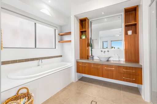 A modern bathroom interior with a bathtub, wooden cabinets, large mirror, and natural light.