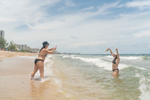 Two young sexy Hispanic girls taking photos of each other at the beach