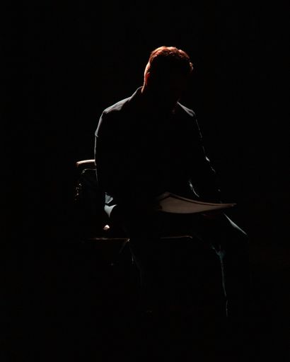 A silhouette of a man sitting on the chair and reading a newspaper in a black room
