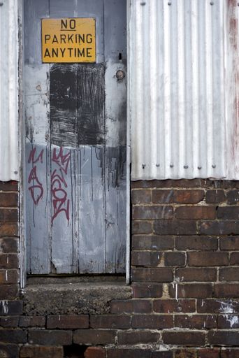 A vertical shot of an old dirty metal door with a yellow "No Parking Anytime" sign